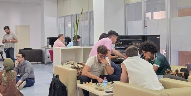 A photo of students during free time at Boğaziçi University, with some playing chess and the piano while others chat, study and socialize.